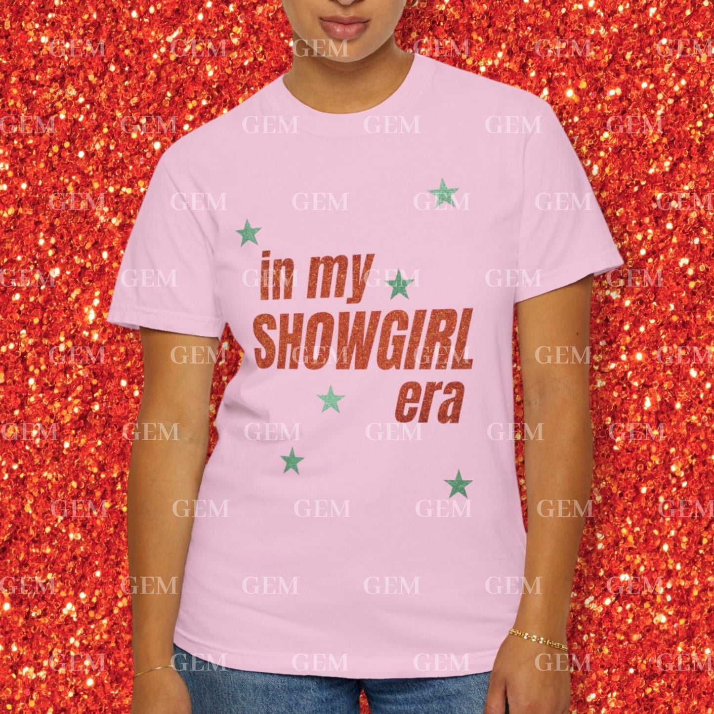 Person wearing a pink t-shirt with 'in my showgirl era' text on a glittery red background