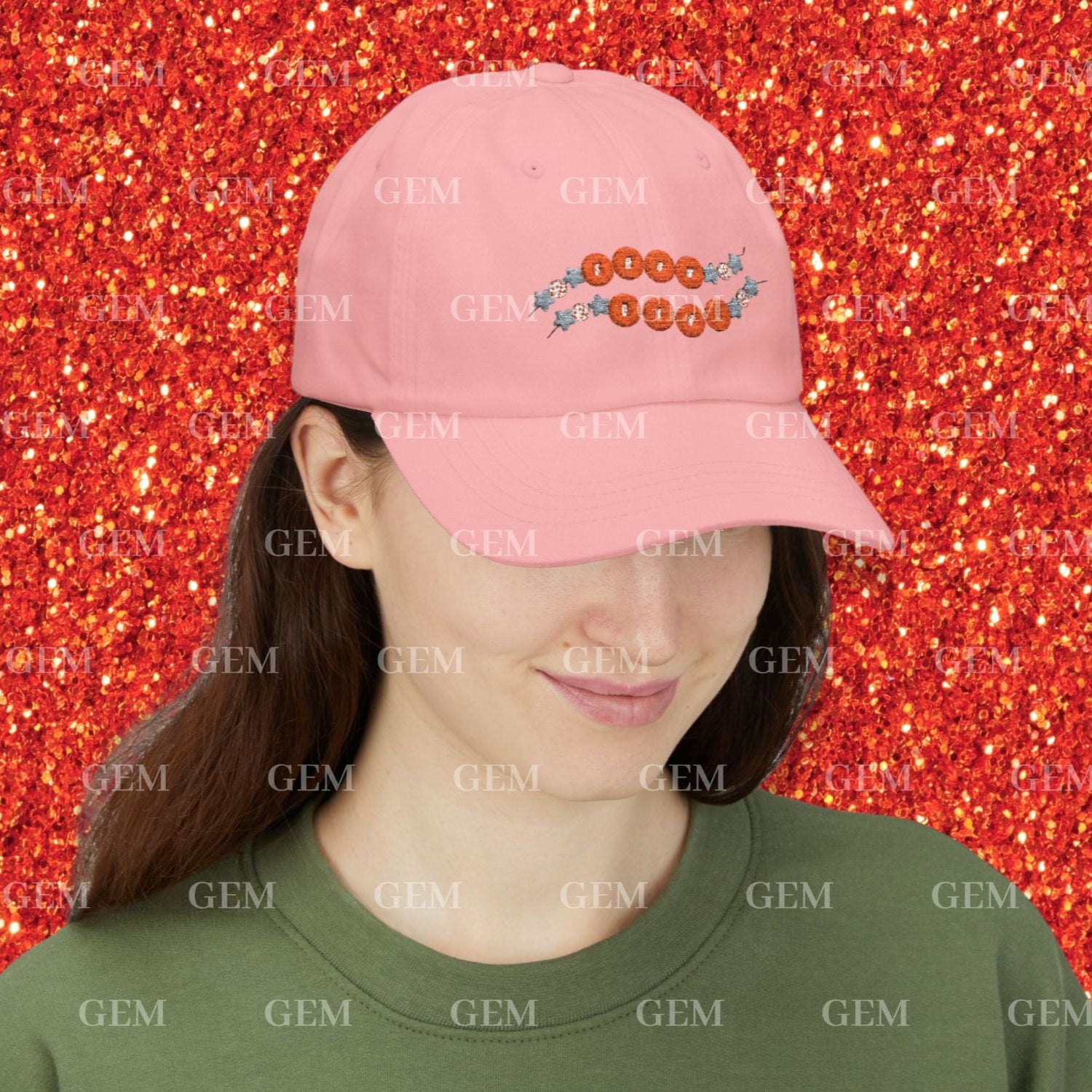 Person wearing a pink cap with friendship bracelet design against a red glittery background