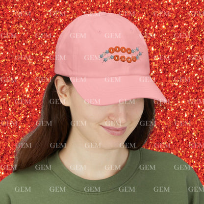 Person wearing a pink cap with friendship bracelet design against a red glittery background